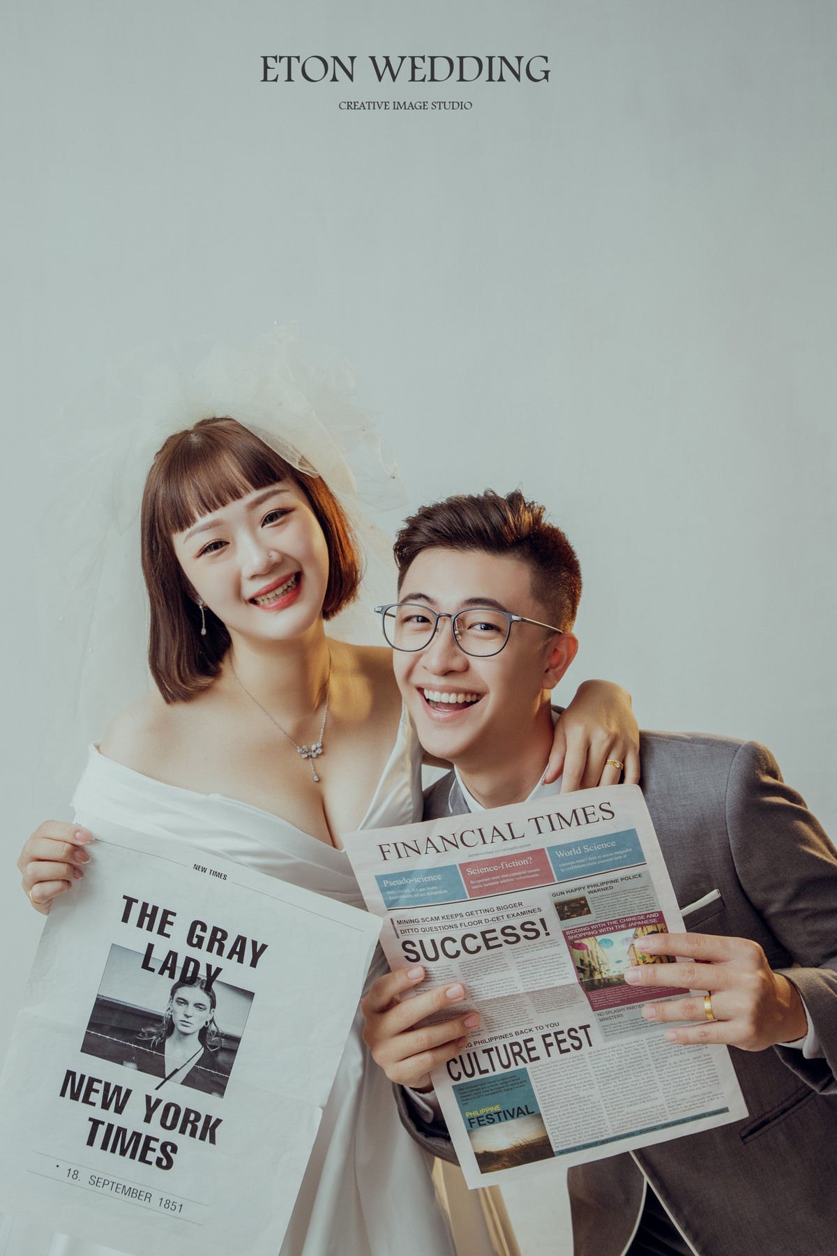 一個短髮可愛新娘跟新郎手上拿著報紙，面對鏡頭燦笑的可愛婚紗照